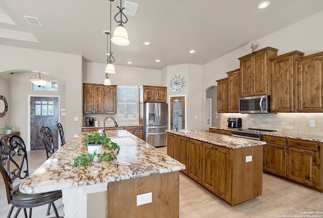 kitchen with a kitchen island with sink, stainless steel appliances, hanging light fixtures, and light hardwood / wood-style floors