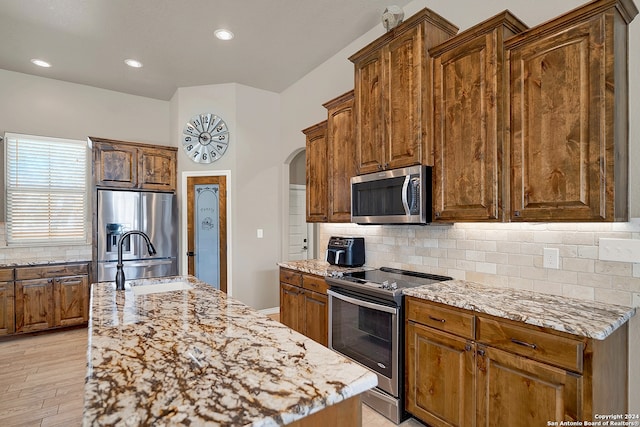 kitchen with stainless steel appliances, sink, tasteful backsplash, an island with sink, and light wood-type flooring