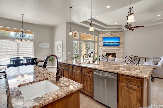 kitchen featuring stainless steel dishwasher, a fireplace, a center island with sink, and sink