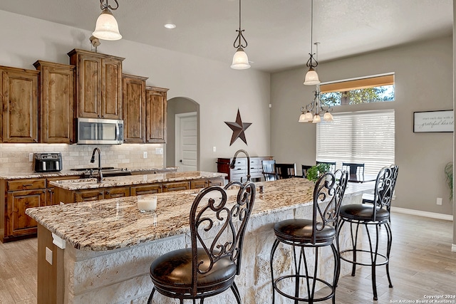 kitchen with light hardwood / wood-style flooring, pendant lighting, light stone countertops, and a spacious island