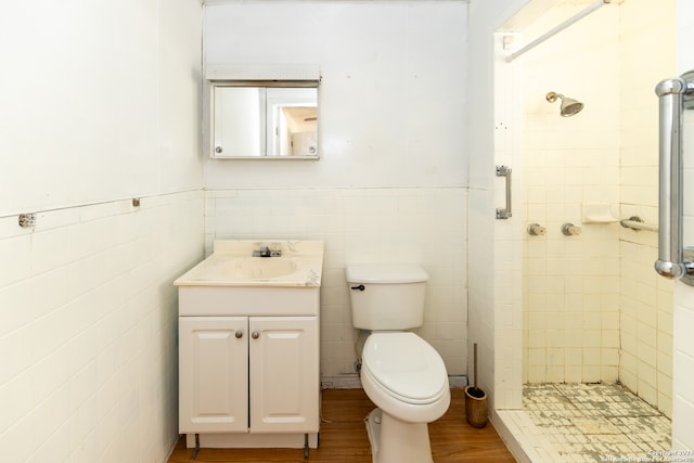 bathroom with tile walls, a tile shower, vanity, hardwood / wood-style flooring, and toilet