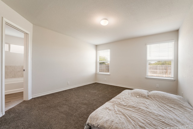 bedroom with connected bathroom, multiple windows, a textured ceiling, and dark colored carpet