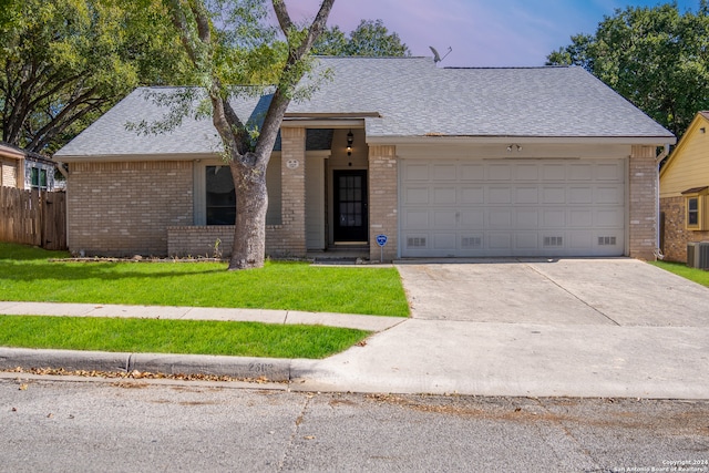 ranch-style house with central air condition unit, a garage, and a yard