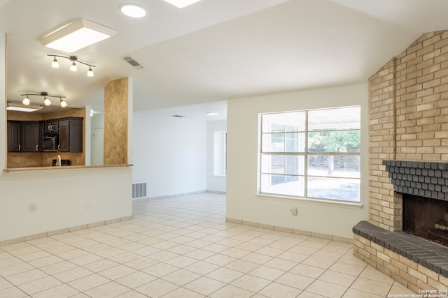 unfurnished living room with brick wall, vaulted ceiling, light tile patterned floors, and a brick fireplace