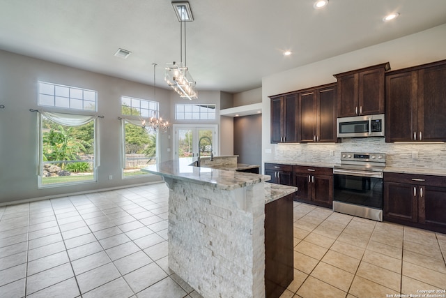 kitchen featuring stainless steel appliances, light stone countertops, light tile patterned floors, an island with sink, and a notable chandelier