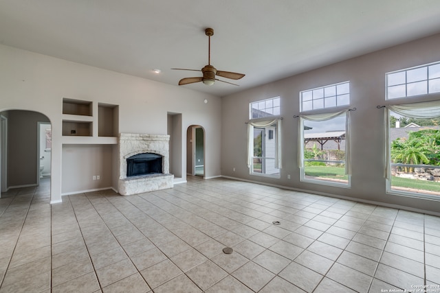 unfurnished living room with a premium fireplace, built in features, light tile patterned floors, and ceiling fan