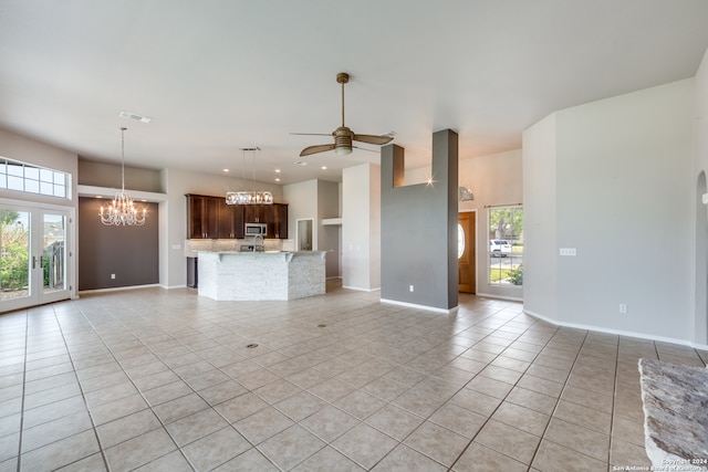 unfurnished living room with ceiling fan with notable chandelier, a wealth of natural light, and light tile patterned floors