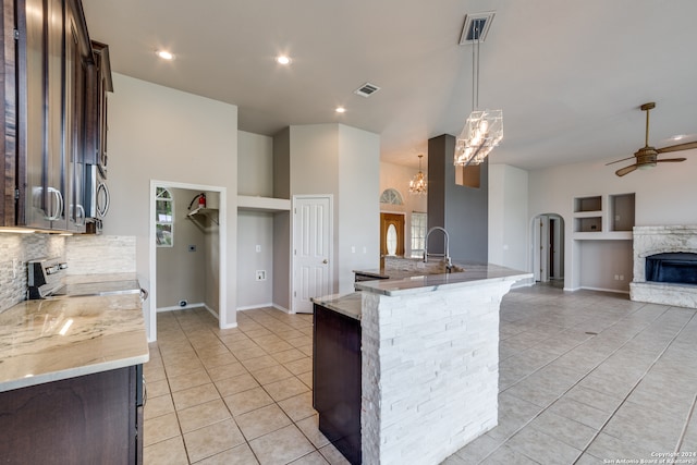 kitchen featuring built in shelves, backsplash, dark brown cabinetry, light stone countertops, and hanging light fixtures