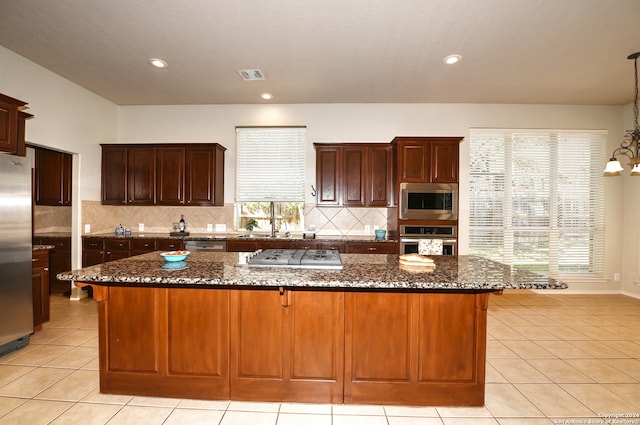 kitchen featuring appliances with stainless steel finishes, tasteful backsplash, dark stone countertops, a kitchen island, and pendant lighting