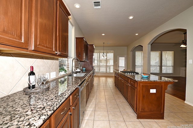 kitchen with stainless steel appliances, a kitchen island, sink, dark stone countertops, and ceiling fan