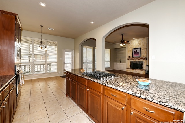 kitchen featuring pendant lighting, ceiling fan with notable chandelier, stainless steel appliances, and dark stone countertops