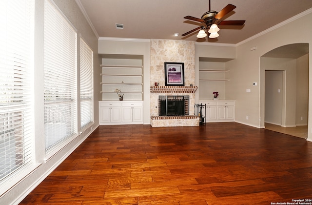 unfurnished living room with built in features, hardwood / wood-style floors, crown molding, and a fireplace