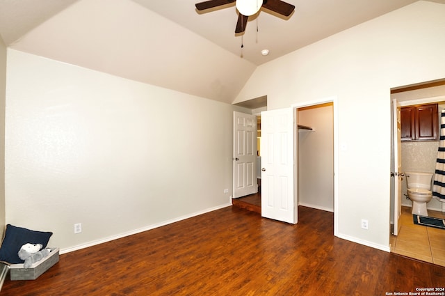 unfurnished bedroom featuring ensuite bathroom, ceiling fan, a walk in closet, dark wood-type flooring, and vaulted ceiling