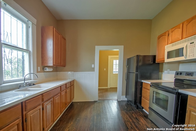 kitchen with dark hardwood / wood-style flooring, black fridge, stainless steel range with electric cooktop, and sink