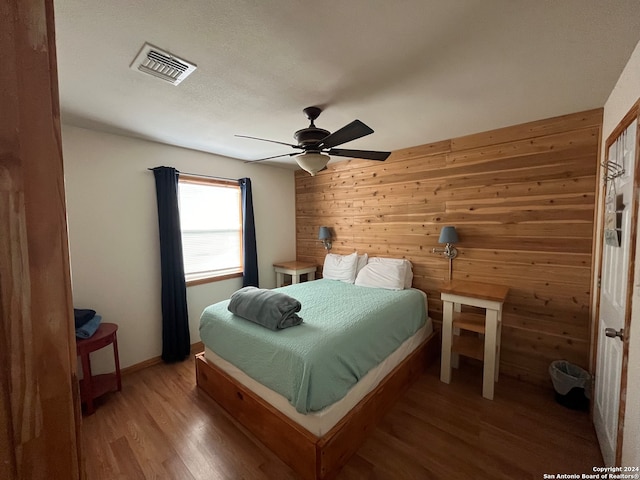 bedroom featuring hardwood / wood-style flooring, ceiling fan, and wood walls