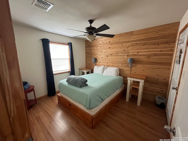 bedroom with hardwood / wood-style flooring, ceiling fan, and wood walls