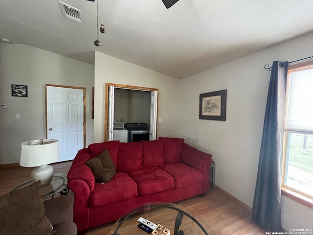 living room with independent washer and dryer, light hardwood / wood-style flooring, and vaulted ceiling