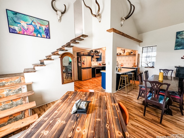 dining space featuring light wood-type flooring, indoor bar, and high vaulted ceiling