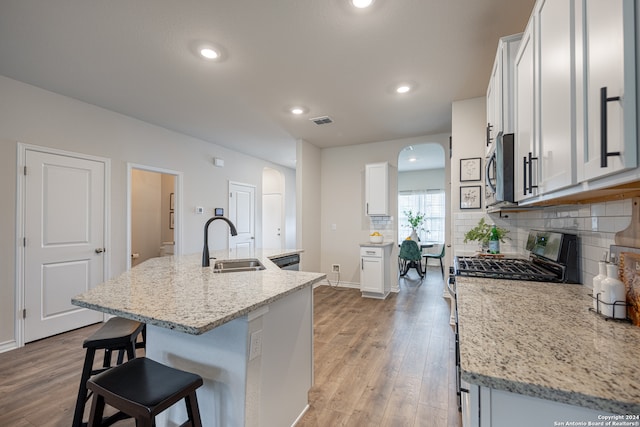 kitchen with appliances with stainless steel finishes, white cabinetry, sink, an island with sink, and light stone counters