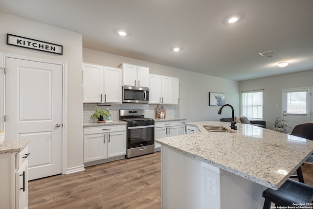 kitchen featuring appliances with stainless steel finishes, sink, tasteful backsplash, white cabinetry, and an island with sink