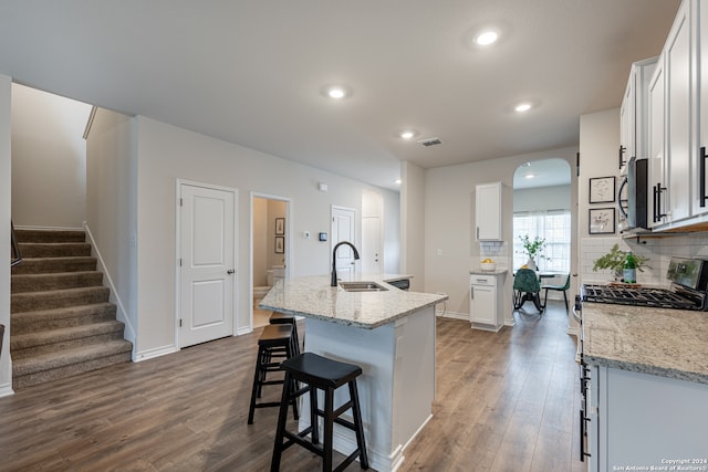 kitchen with white cabinets, light stone counters, a center island with sink, and sink