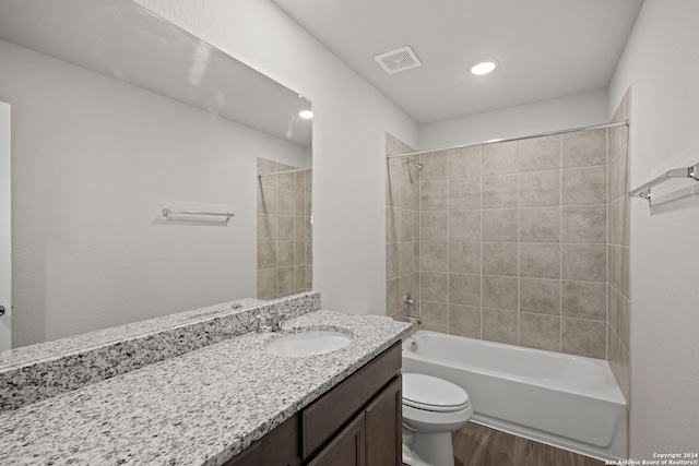 full bathroom with tiled shower / bath combo, vanity, hardwood / wood-style flooring, and toilet