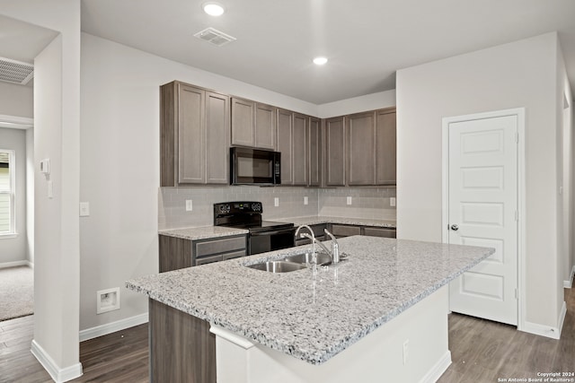 kitchen with a center island with sink, sink, black appliances, and light stone counters