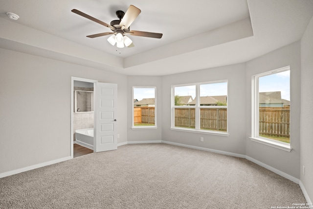 unfurnished bedroom with ceiling fan, ensuite bath, carpet flooring, and a raised ceiling