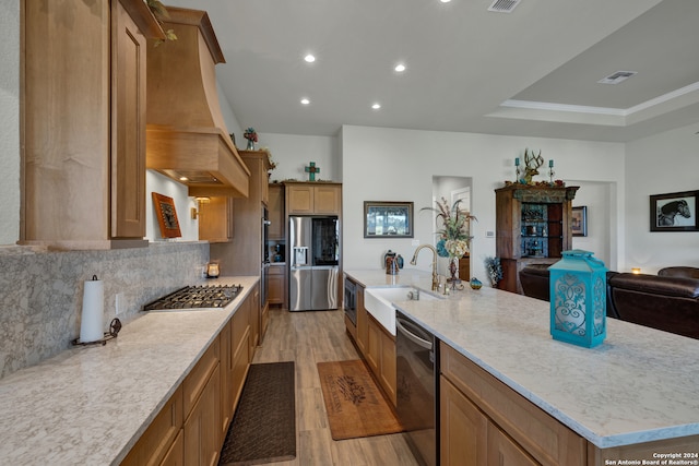 kitchen featuring light hardwood / wood-style flooring, sink, appliances with stainless steel finishes, a large island with sink, and premium range hood