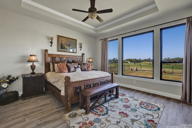 bedroom with ornamental molding, a tray ceiling, hardwood / wood-style floors, and ceiling fan