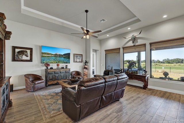 living room with light hardwood / wood-style floors, ceiling fan, and a tray ceiling