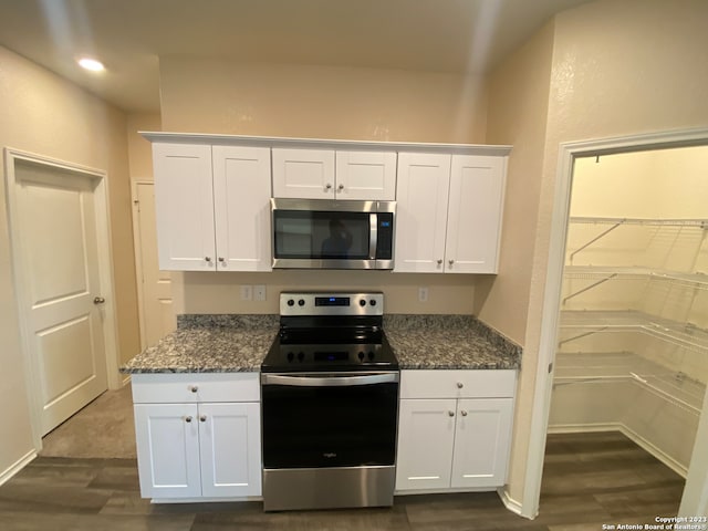 kitchen with white cabinetry, appliances with stainless steel finishes, dark stone countertops, and dark hardwood / wood-style flooring