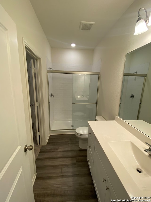 bathroom with wood-type flooring, vanity, a shower with door, and toilet