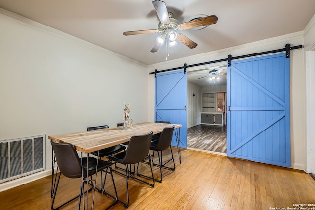 dining space featuring ornamental molding, wood-type flooring, a barn door, and ceiling fan