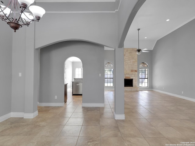 unfurnished living room featuring a stone fireplace, ceiling fan with notable chandelier, light tile patterned floors, and crown molding