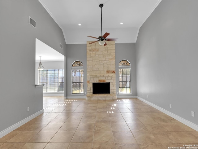 unfurnished living room with ceiling fan, light tile patterned floors, high vaulted ceiling, a stone fireplace, and crown molding