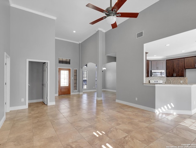 unfurnished living room with ornamental molding, a towering ceiling, ceiling fan, and light tile patterned flooring