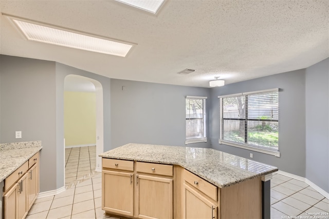 kitchen featuring a textured ceiling, light tile patterned floors, a kitchen island, light stone countertops, and light brown cabinets