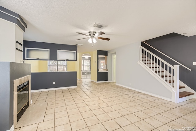 unfurnished living room with a textured ceiling, ceiling fan, and light tile patterned floors