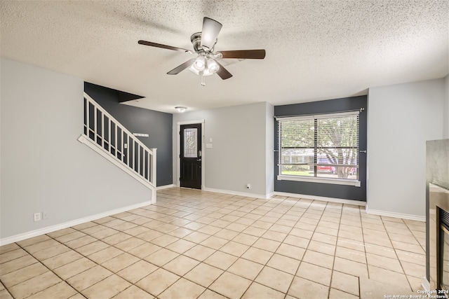 unfurnished living room with ceiling fan, a textured ceiling, light tile patterned floors, and a tiled fireplace