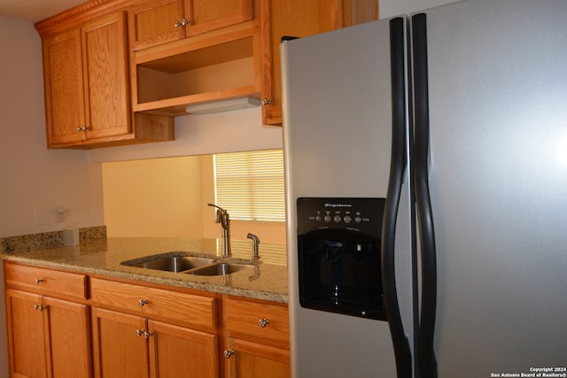 kitchen featuring stainless steel refrigerator with ice dispenser, sink, and light stone countertops