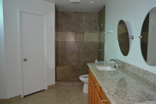 bathroom with toilet, tiled shower, vanity, and tile patterned floors