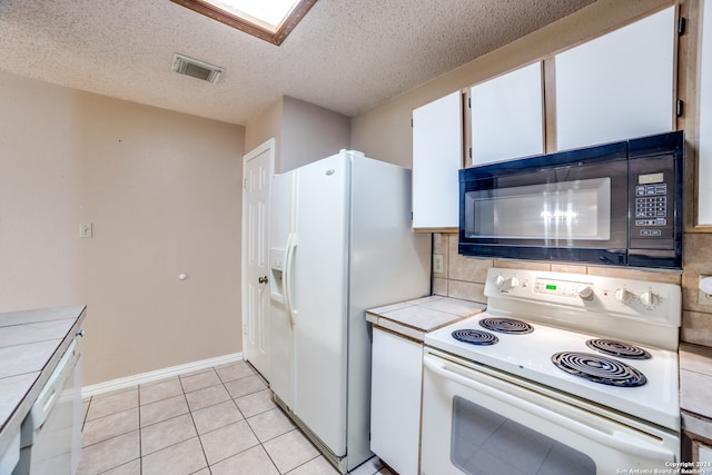 kitchen featuring tile counters, a textured ceiling, light tile patterned flooring, white cabinetry, and white appliances