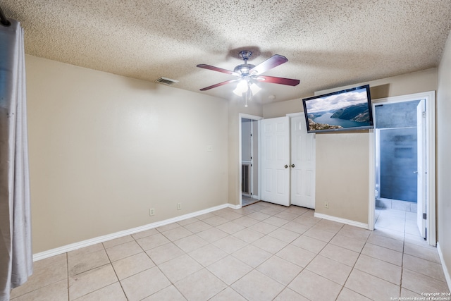 unfurnished bedroom with a textured ceiling, connected bathroom, ceiling fan, and light tile patterned flooring