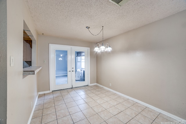 unfurnished dining area with french doors, a notable chandelier, a textured ceiling, and light tile patterned floors