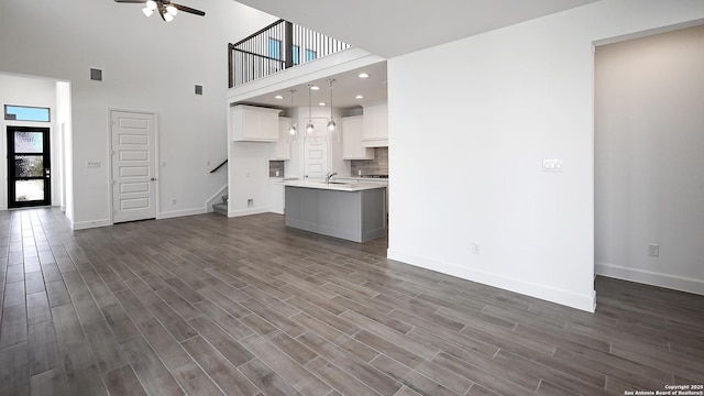 unfurnished living room featuring dark wood-style flooring, a ceiling fan, and baseboards