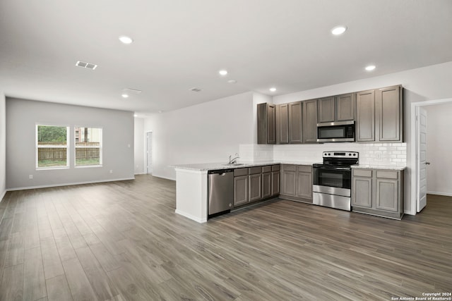 kitchen featuring tasteful backsplash, kitchen peninsula, appliances with stainless steel finishes, and dark hardwood / wood-style floors