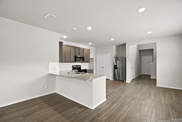 kitchen with stainless steel appliances, hardwood / wood-style floors, kitchen peninsula, light stone countertops, and dark brown cabinets