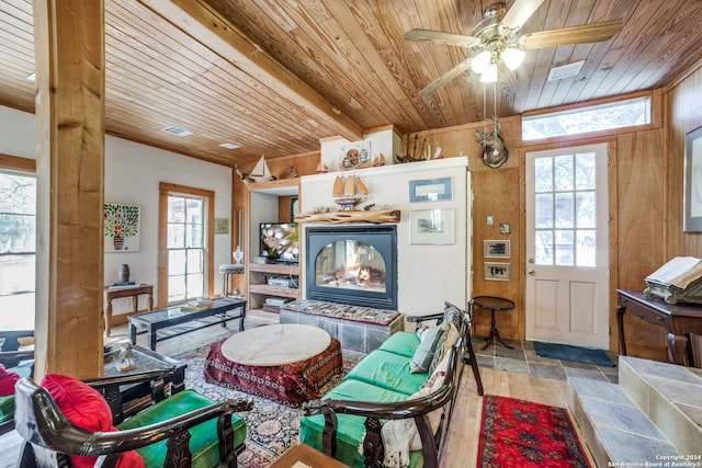 interior space with a tiled fireplace, wood ceiling, wooden walls, and ceiling fan