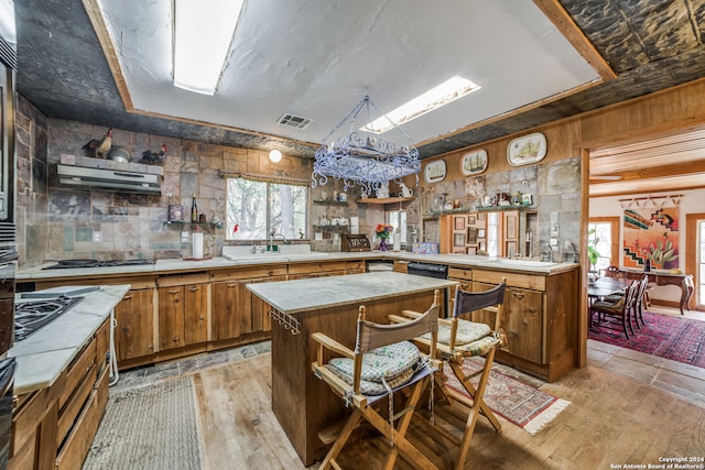 kitchen featuring black gas stovetop, a notable chandelier, tasteful backsplash, a kitchen island, and light wood-type flooring